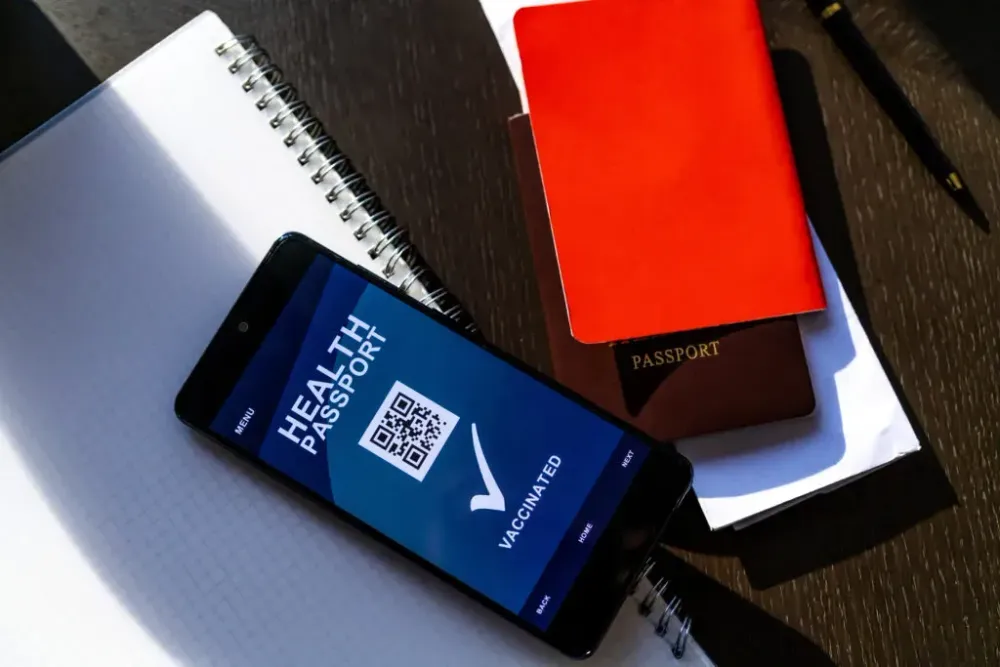 Passport, phone with digital vaccine passport, and graph paper on table